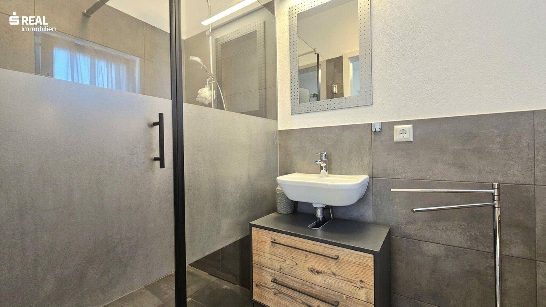 Modernes Badezimmer mit begehbarer Dusche, Einzelwaschbecken und grauen Fliesen.