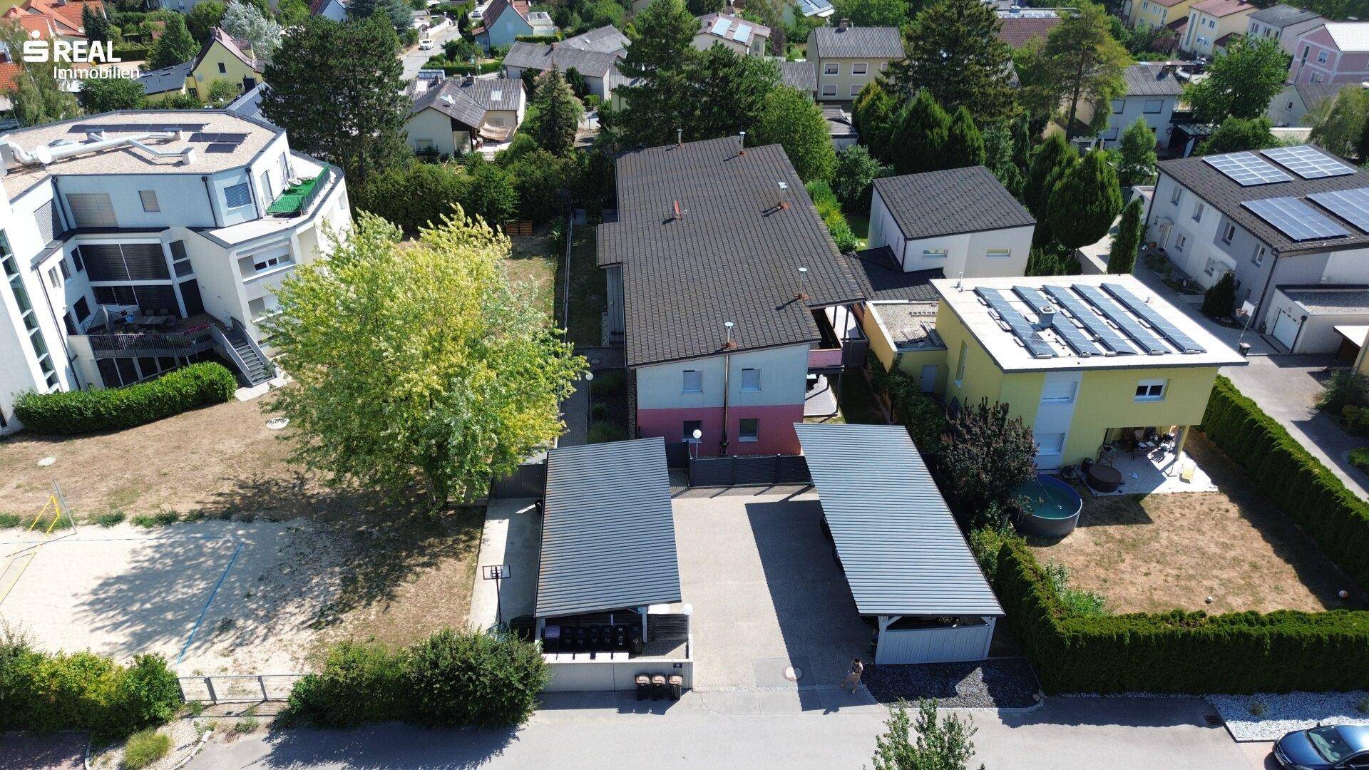 Weitläufige Luftaufnahme des Wohnhauses mit zwei Carports und der umliegenden Wohnsiedlung mit viel Grün.