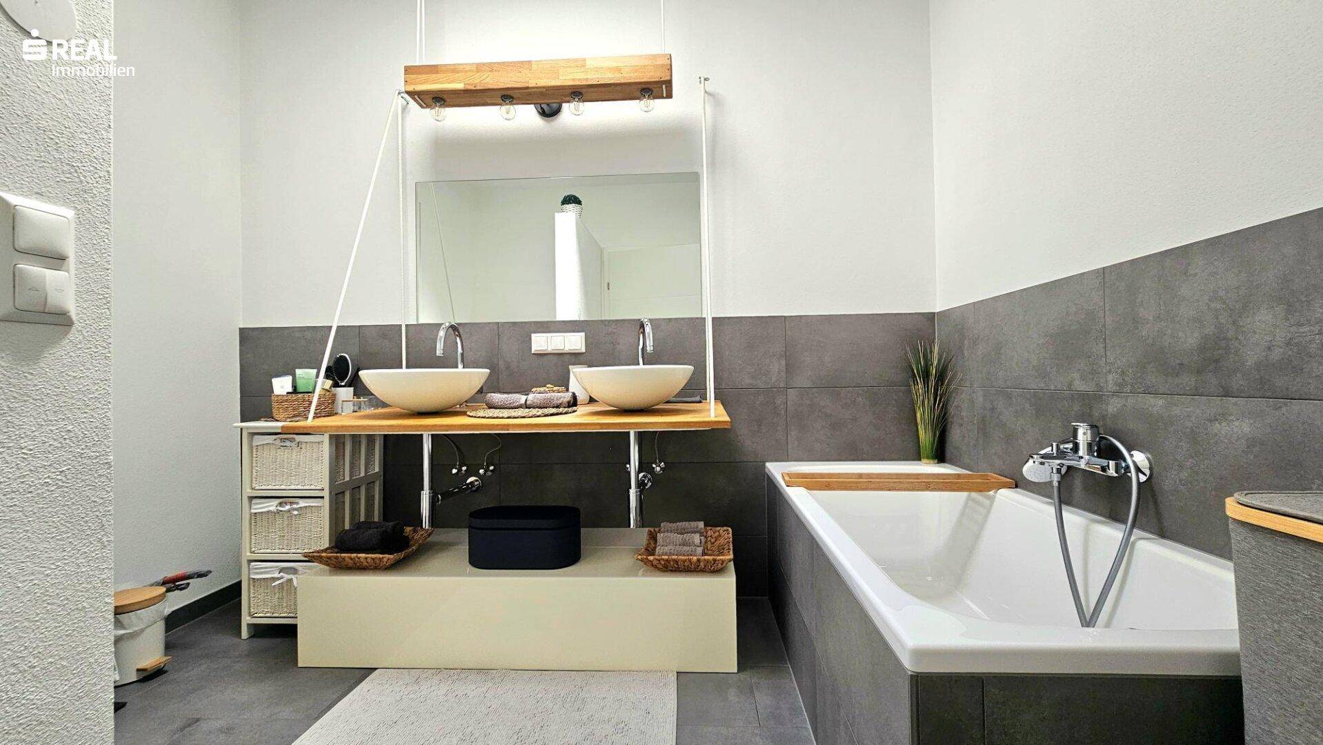 Modernes Badezimmer mit Badewanne, Doppelwaschbecken und grauen Wandfliesen.