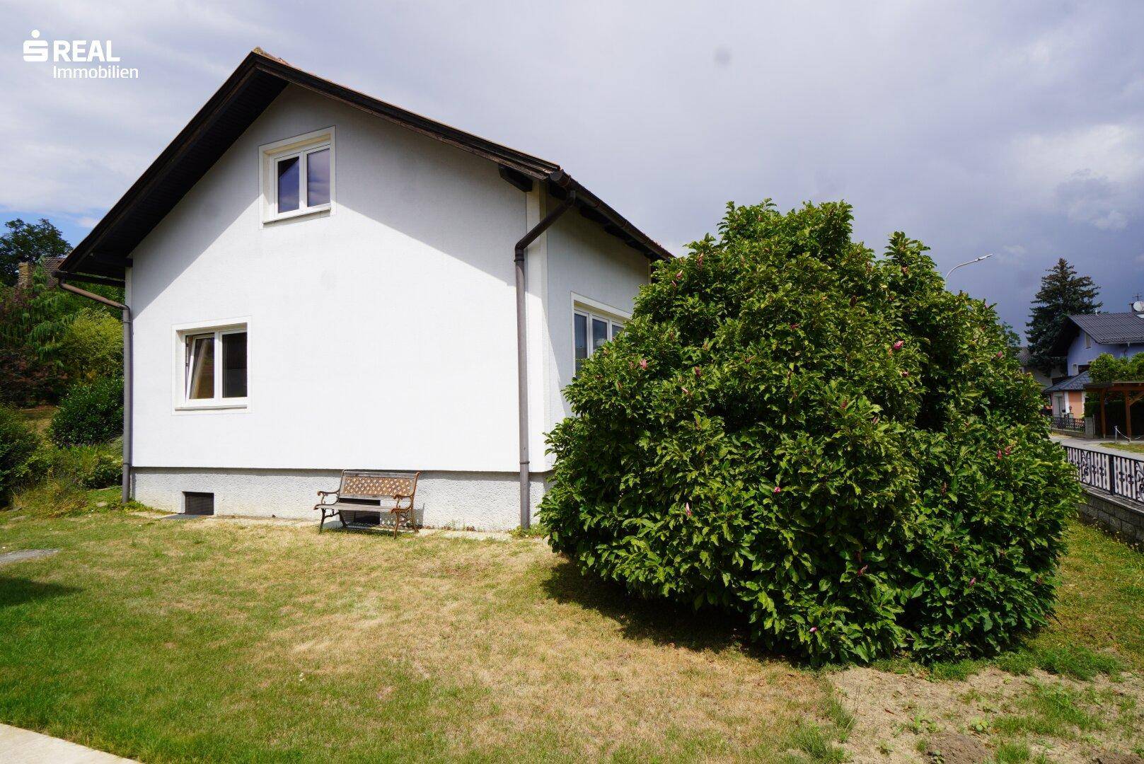 Seitenansicht des Hauses mit Rasenfläche und einem großen Busch im Vordergrund.