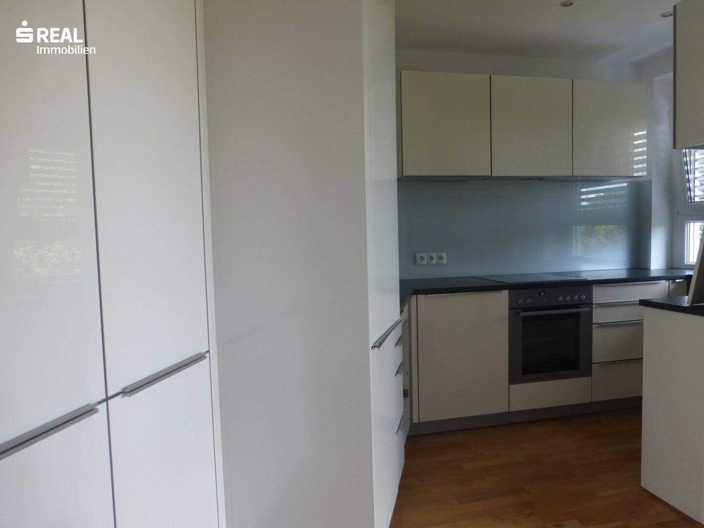 Moderne Küche mit weißen Hochglanzfronten, dunkler Arbeitsplatte und integriertem Backofen.