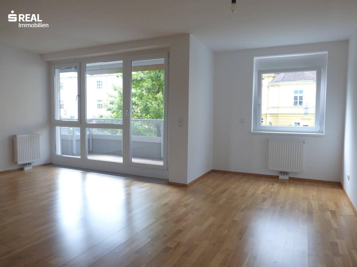 Lichtdurchfluteter Wohnbereich mit Parkettboden und großen Fenstern, die viel Tageslicht hereinlassen.