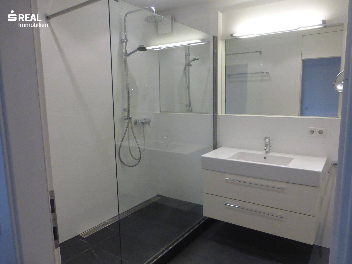 Modernes Badezimmer mit ebenerdiger Dusche, Einzelwaschbecken und großem Spiegel.