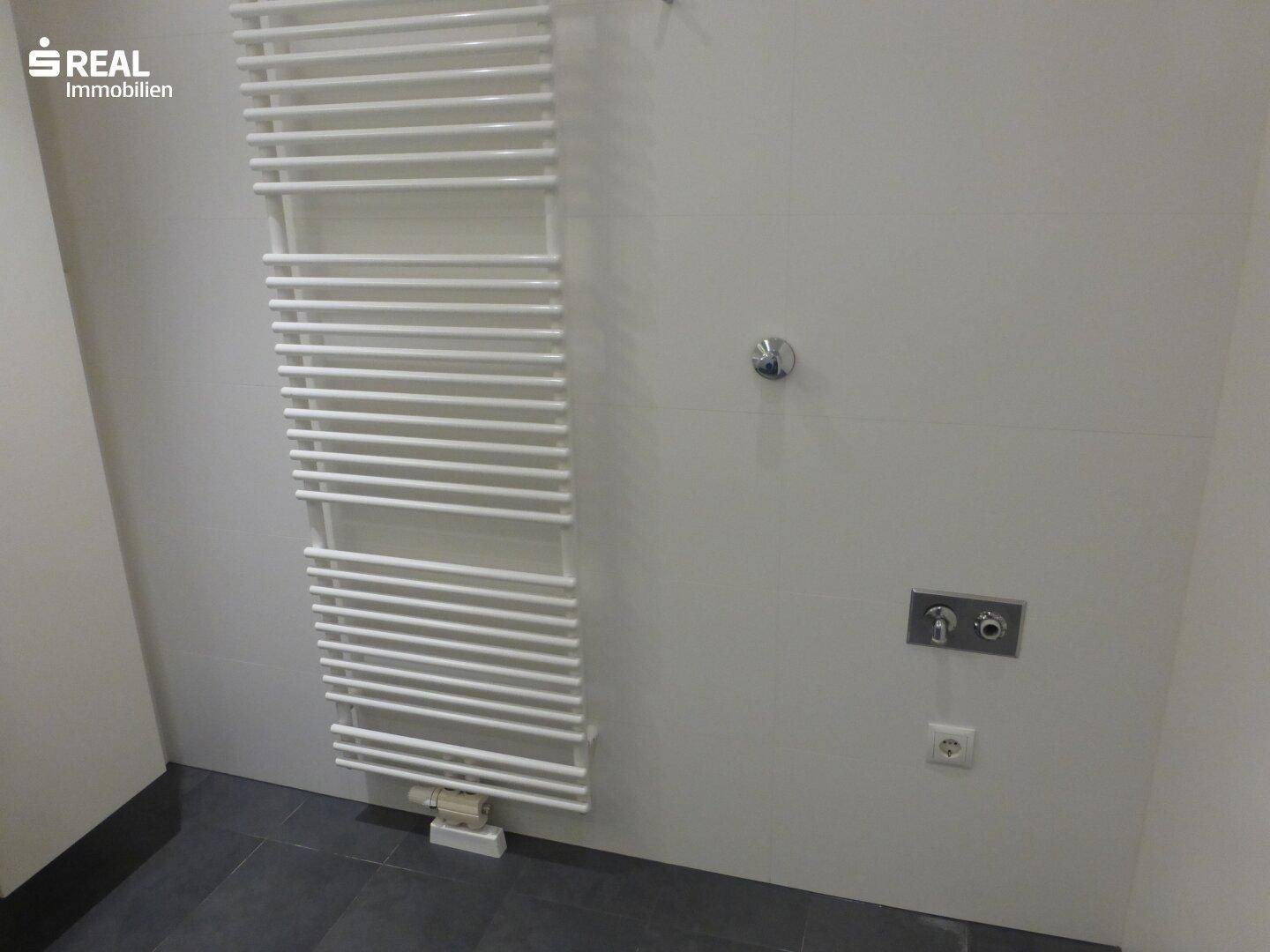 Wand im Badezimmer mit einem beheizten Handtuchhalter und Anschlüssen.