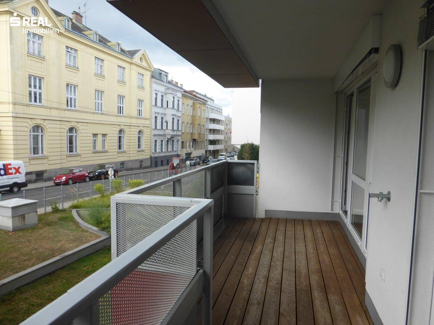 Balkon mit Holzboden und seitlichem Blick auf die belebte Straße und Gebäude.