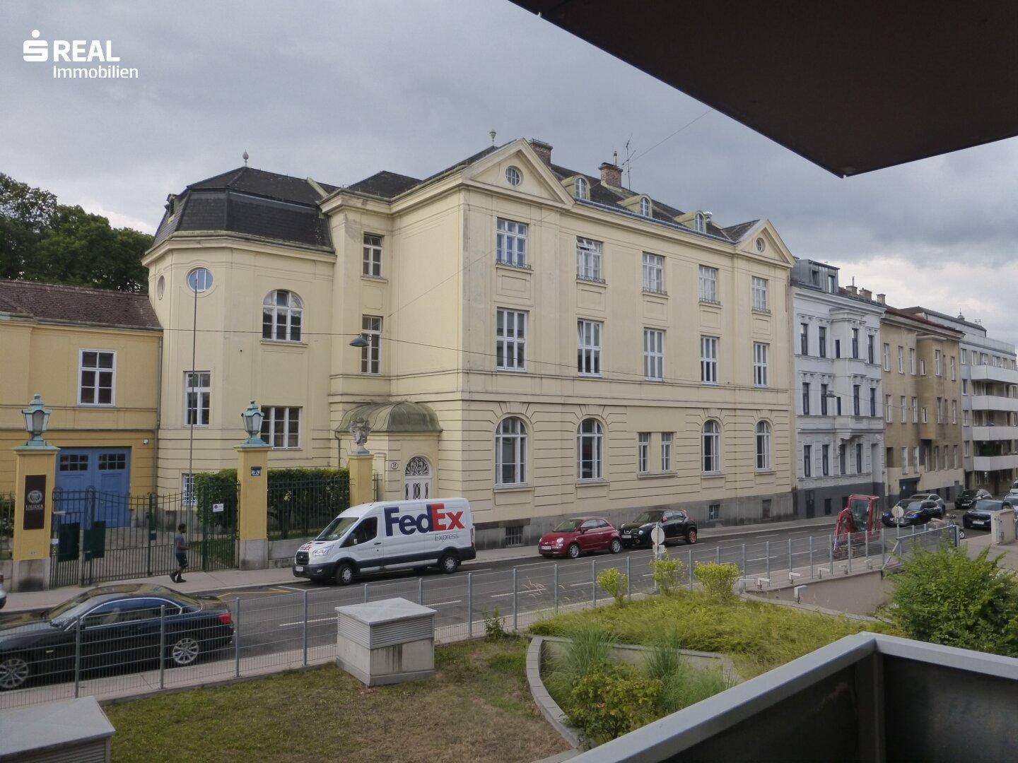 Ausblick von einem Balkon auf ein großes, historisches Gebäude an der Straße.