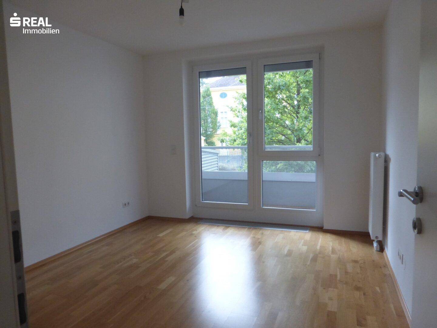 Geräumiges Schlafzimmer mit Parkettboden und großem Fenster mit Blick ins Grüne.