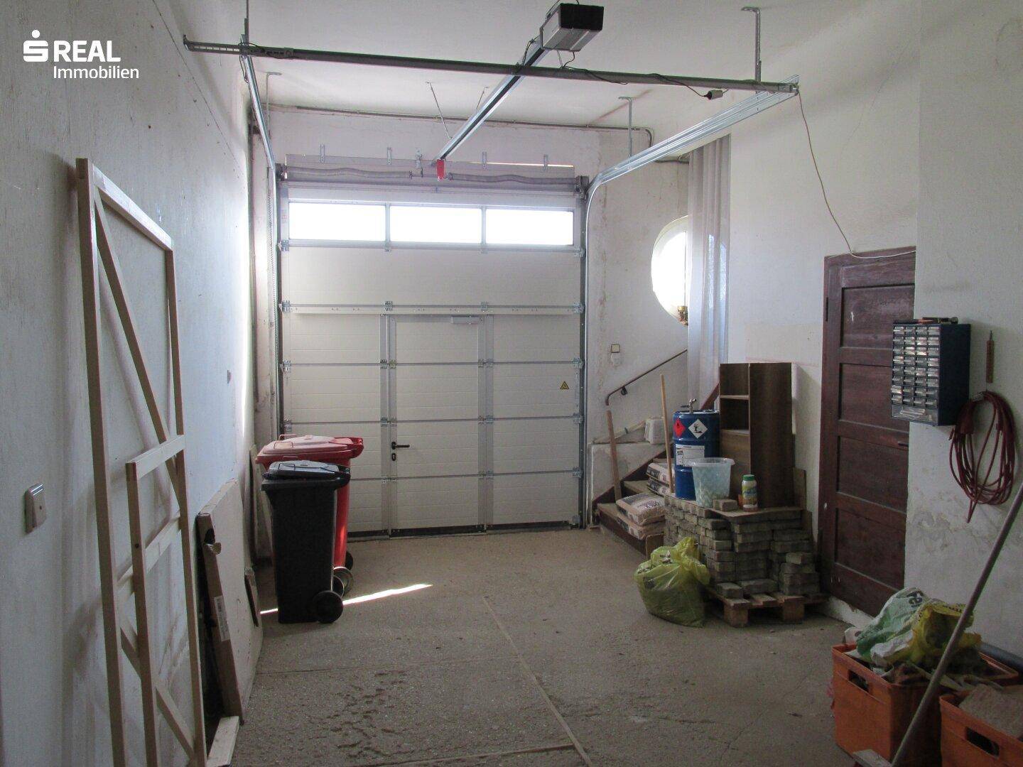 Innenansicht einer geräumigen Garage mit Sektionaltor, Betonboden und Lagerfläche.