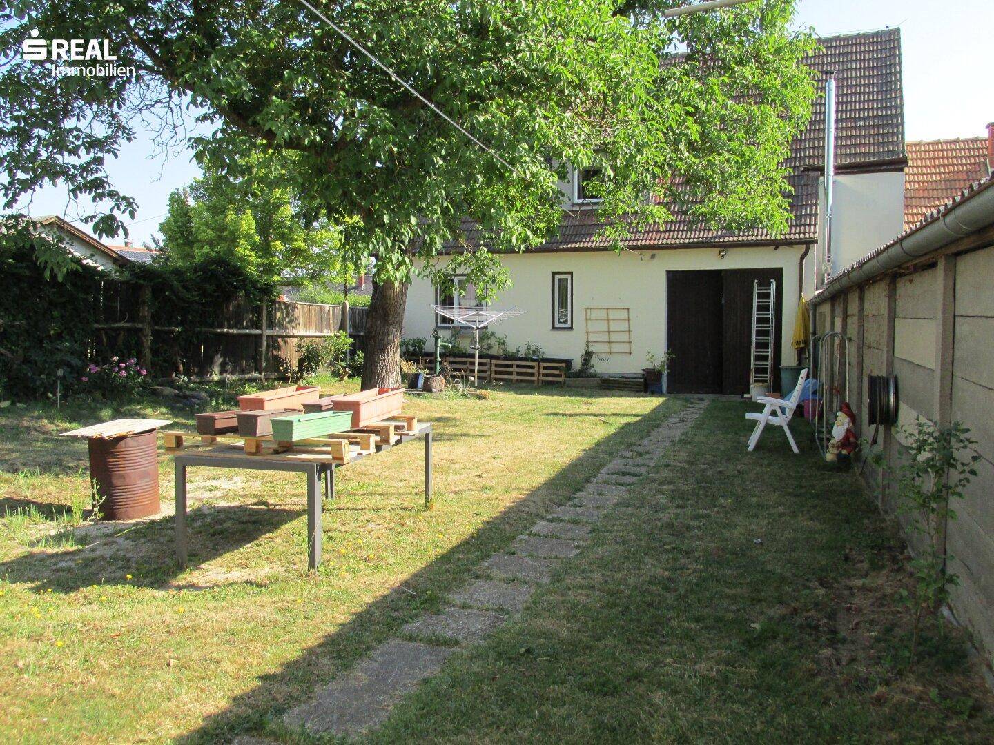 Langer Gartenweg mit Rasenfläche, Bäumen und dem Haus im Hintergrund.