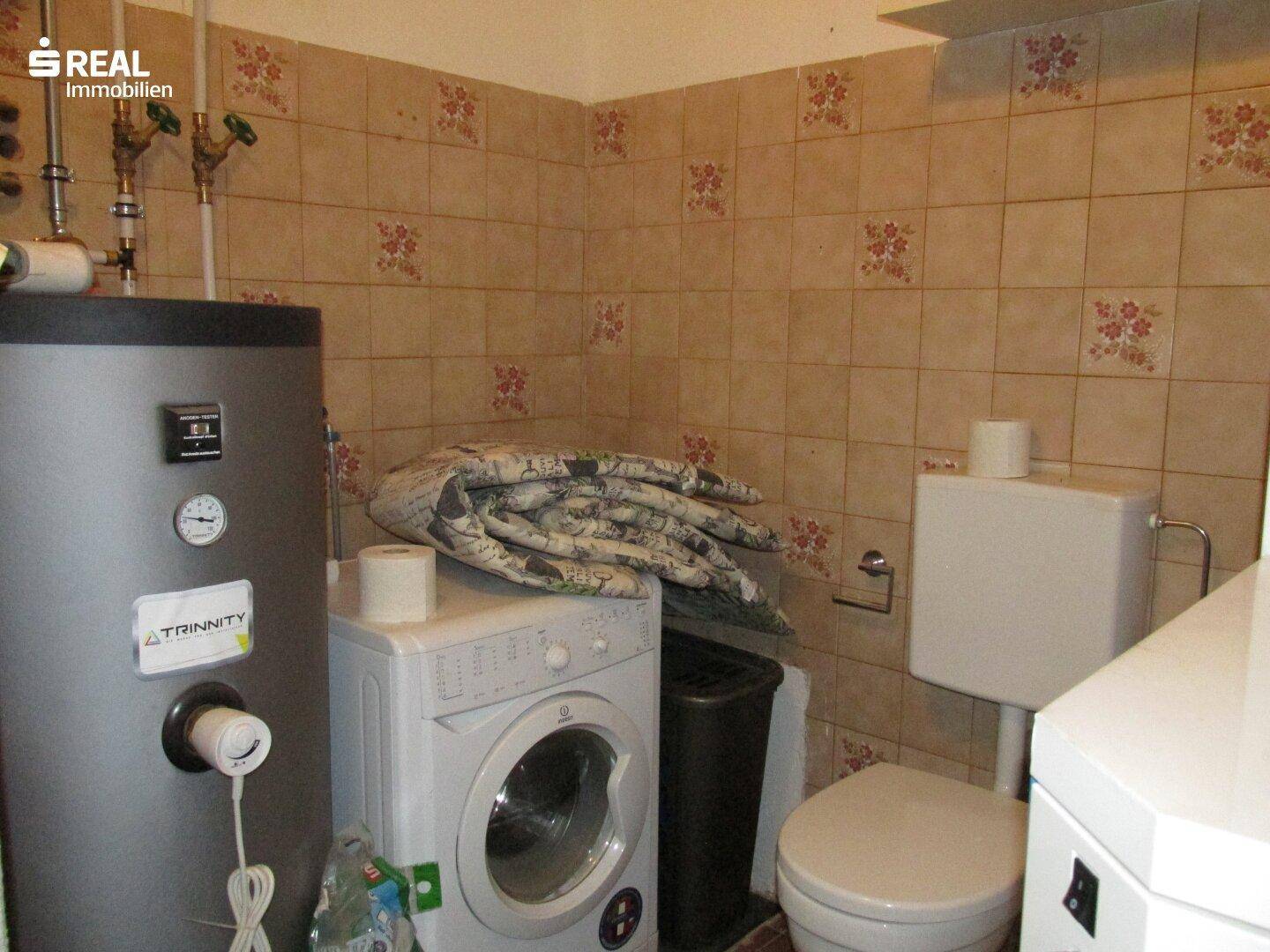 Hauswirtschaftsraum mit Warmwasserboiler, Waschmaschine und WC, praktisch für den täglichen Gebrauch.