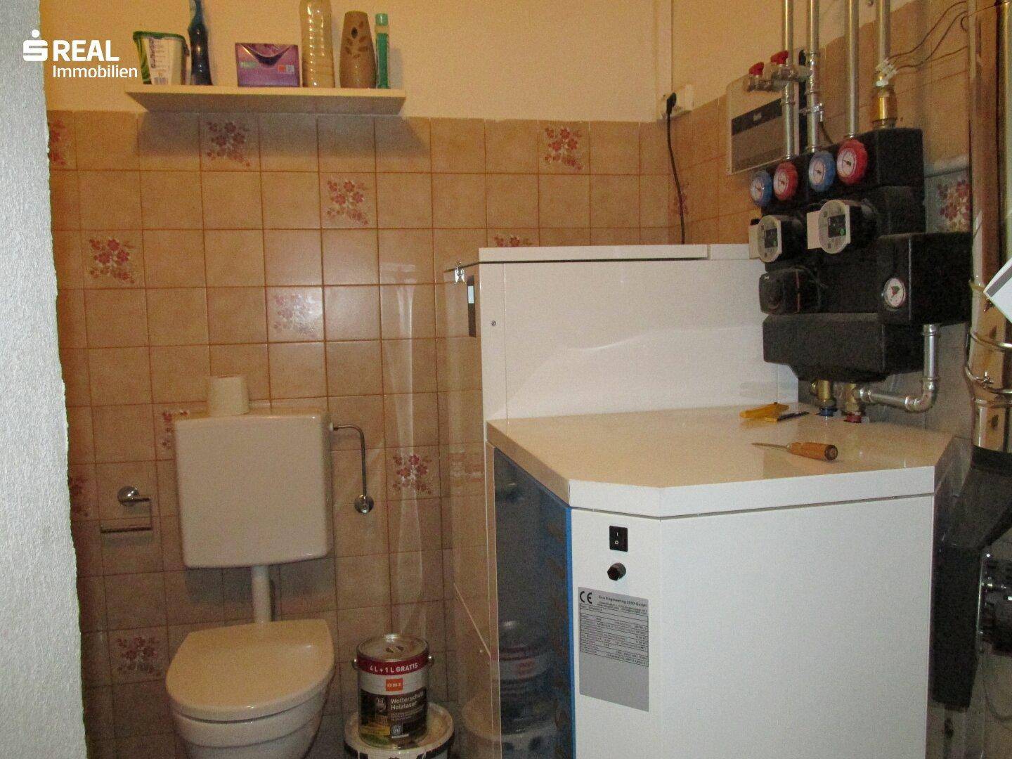 Heizungsraum mit Kessel, Rohren und gefliesten Wänden, der die technische Ausstattung des Hauses zeigt.