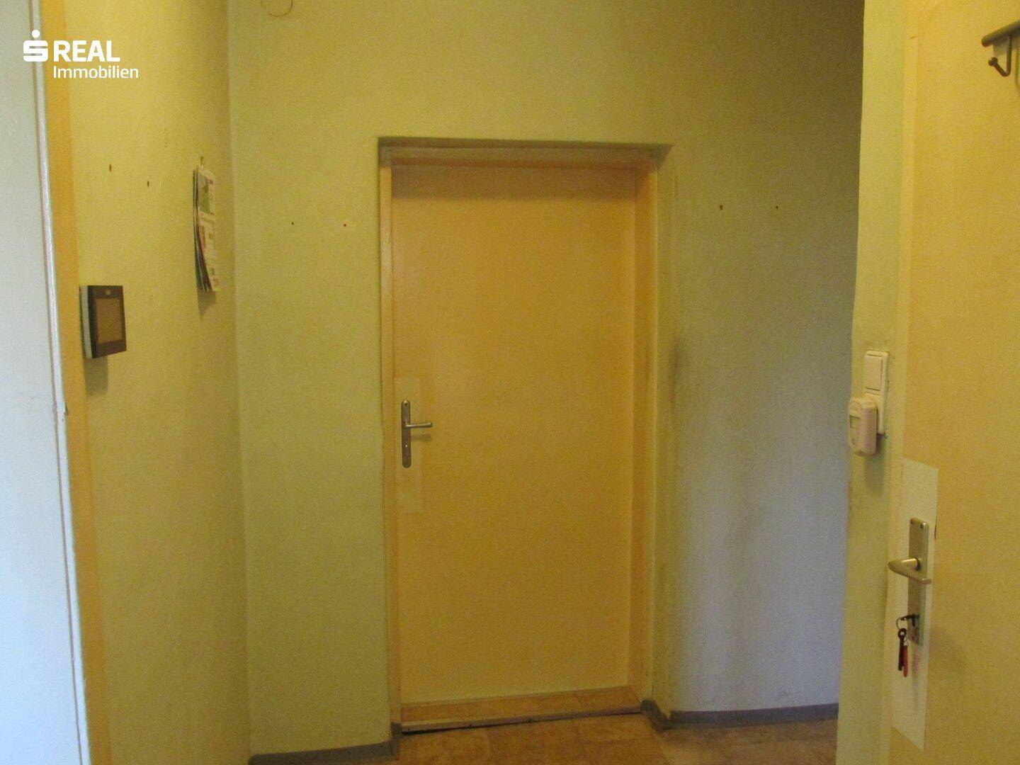 Schmaler Flur mit gelben Wänden und einer Holztür, die zu einem anderen Raum führt.