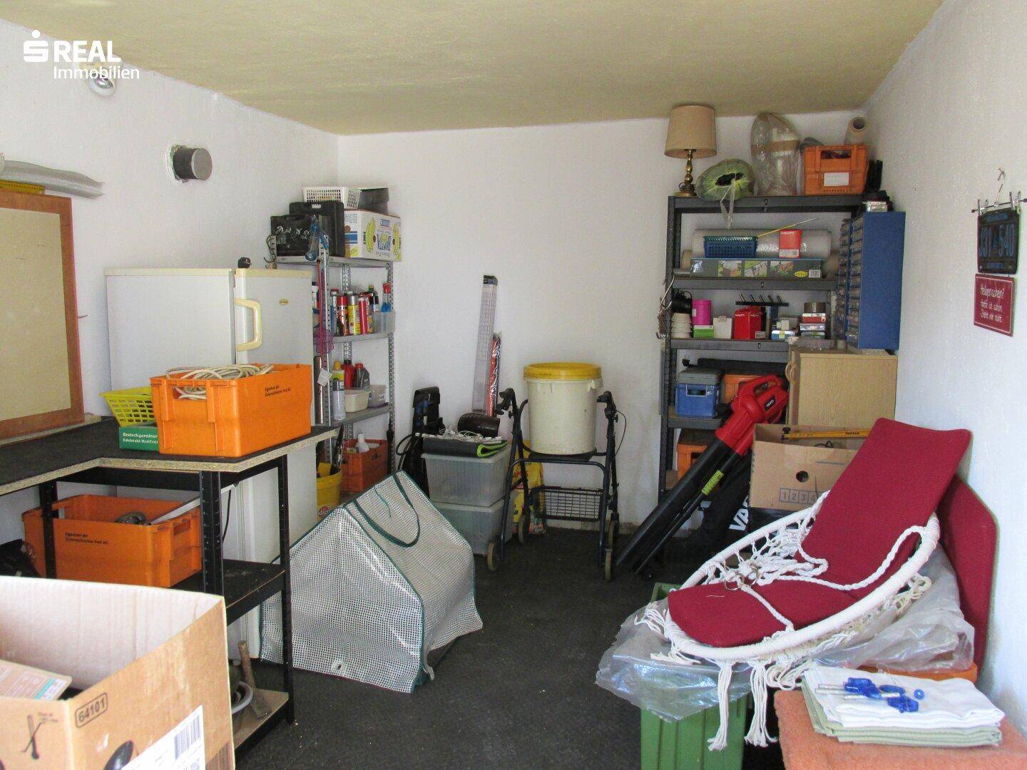 Geräumiger Abstellraum mit Regalen, Kühlschrank und verschiedenen Haushaltsgegenständen.