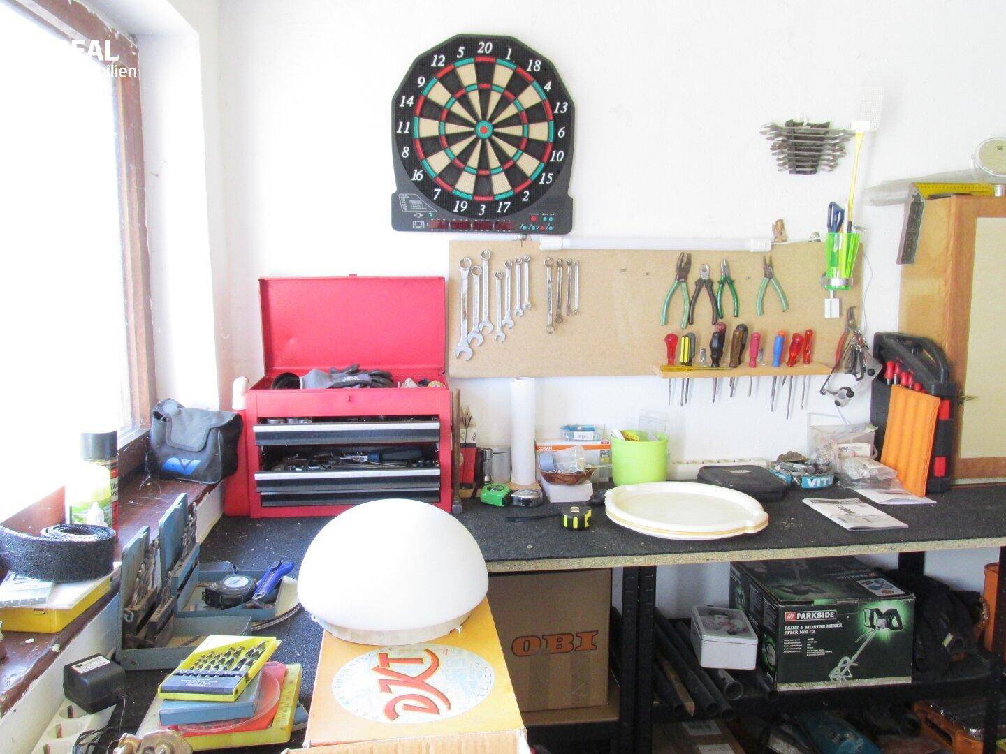 Werkstattbereich mit Werkbank, Werkzeugen an der Wand und einer Dartscheibe.