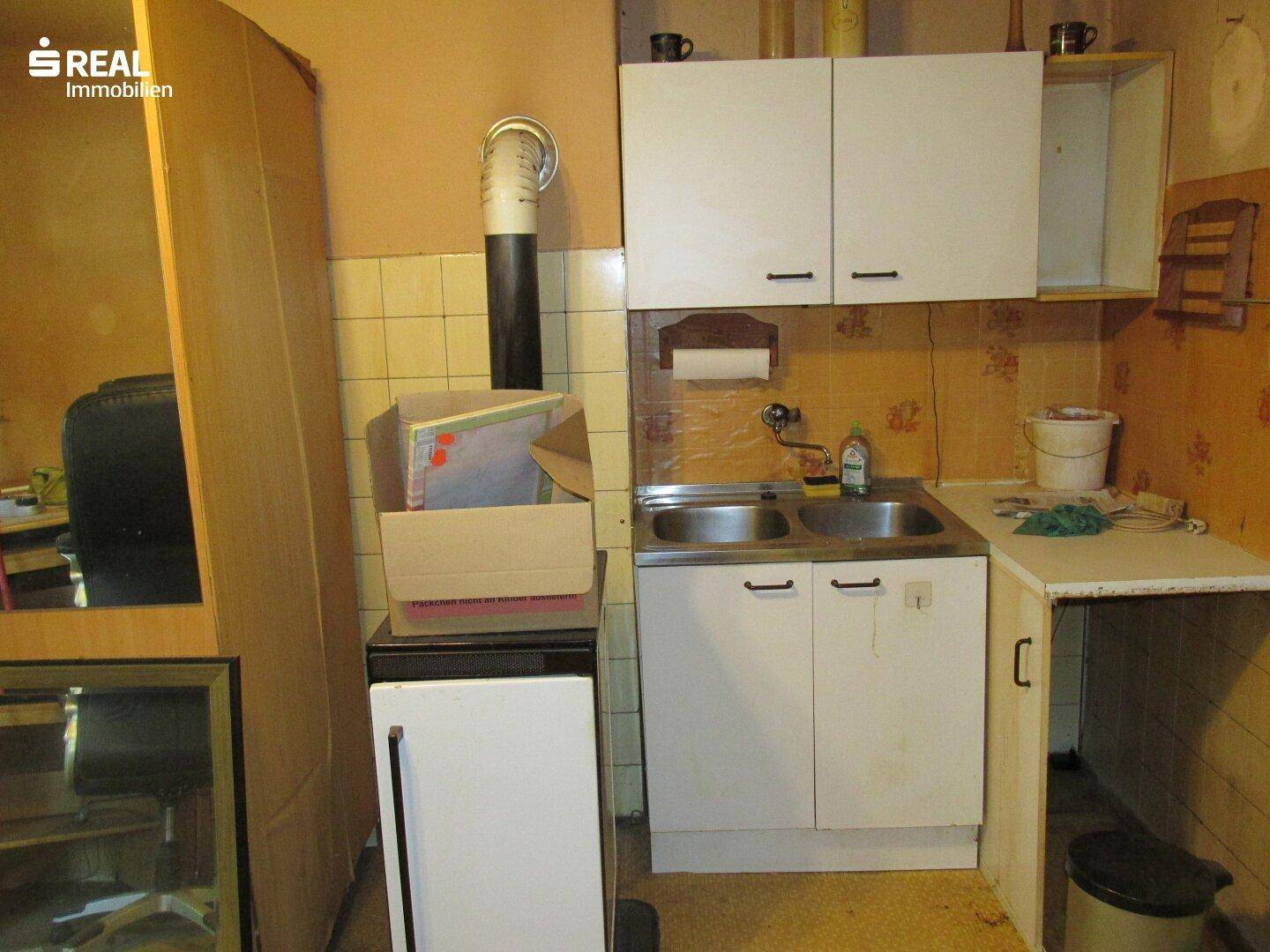 Kleine Küche mit Spülbecken, einfachen weißen Schränken und einem sichtbaren Holzofen für Wärme.