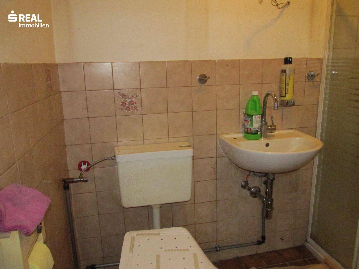 Funktionales Badezimmer mit WC, Waschbecken und beigen Fliesen, die einen älteren Stil aufweisen.