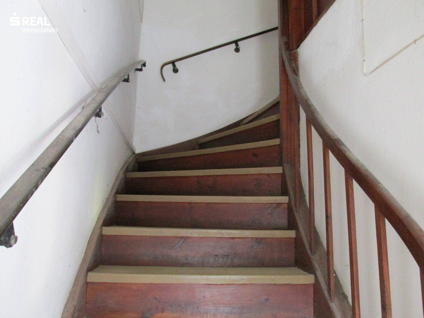 Alte Holztreppe mit Geländer, die in ein oberes Stockwerk führt und den Charme des Gebäudes unterstreicht.