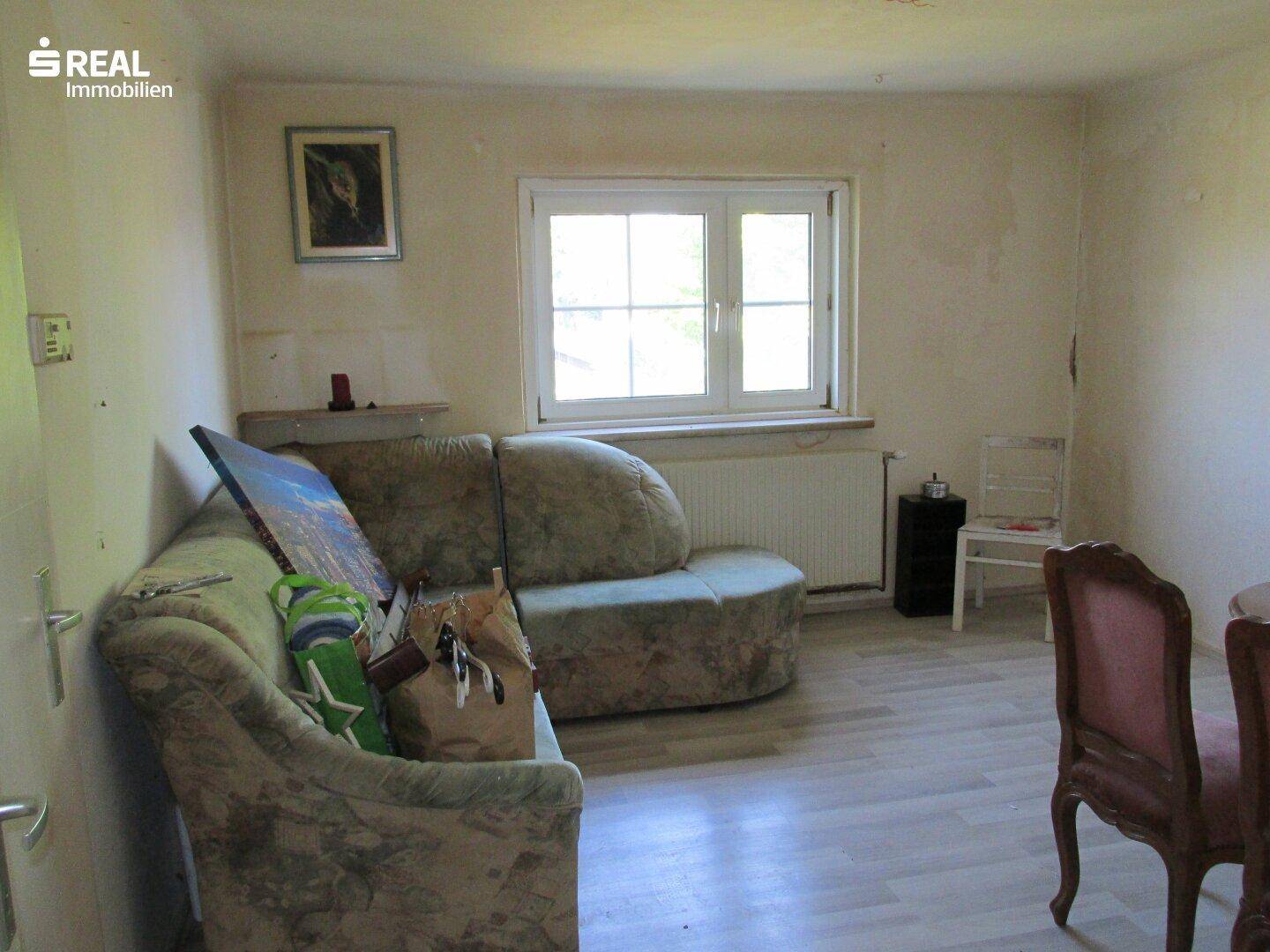 Wohnzimmer mit Sofa, Fenster und hellem Laminatboden, das eine gemütliche Atmosphäre schafft.
