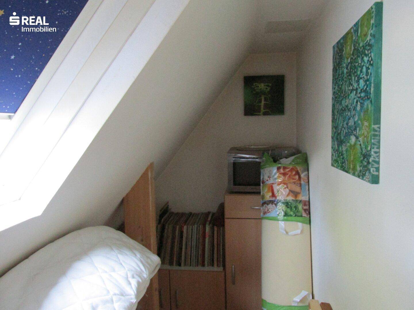 Schlafzimmer im Dachgeschoss mit schrägen Wänden und einem Dachfenster, das für Helligkeit sorgt.