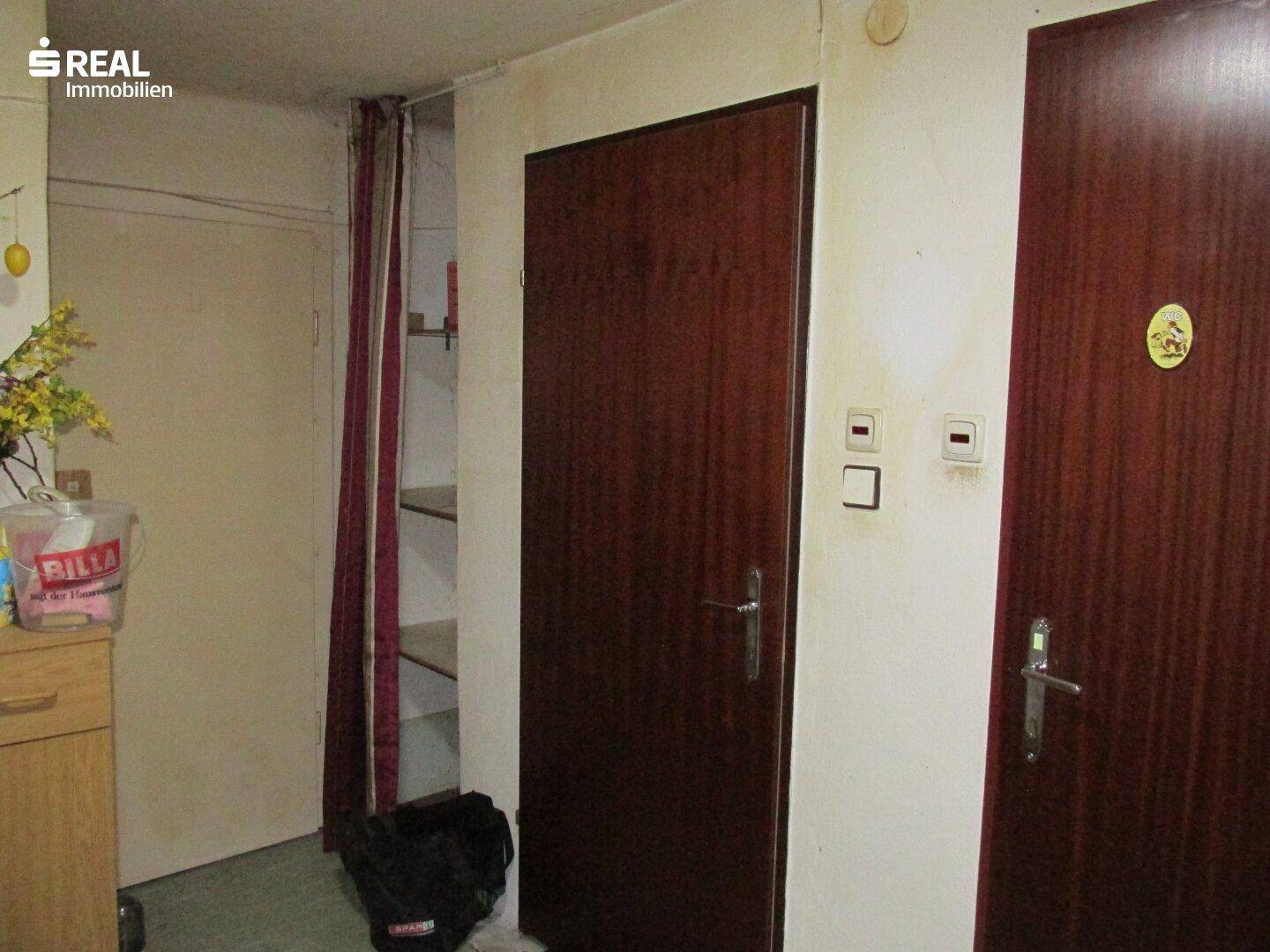 Einfacher Flur mit mehreren Holztüren und einem offenen Regalbereich, der Stauraum bietet.