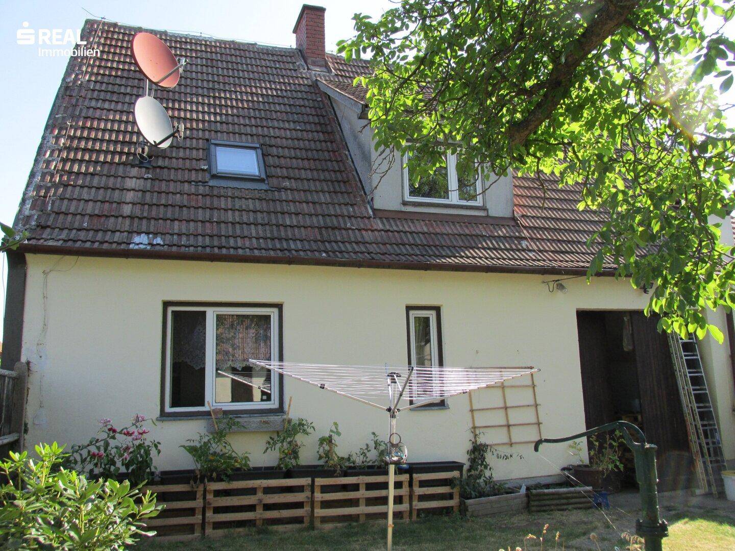 Rückseite des Hauses mit Ziegeldach, Dachgaube und Wäschespinne im sonnigen Garten.