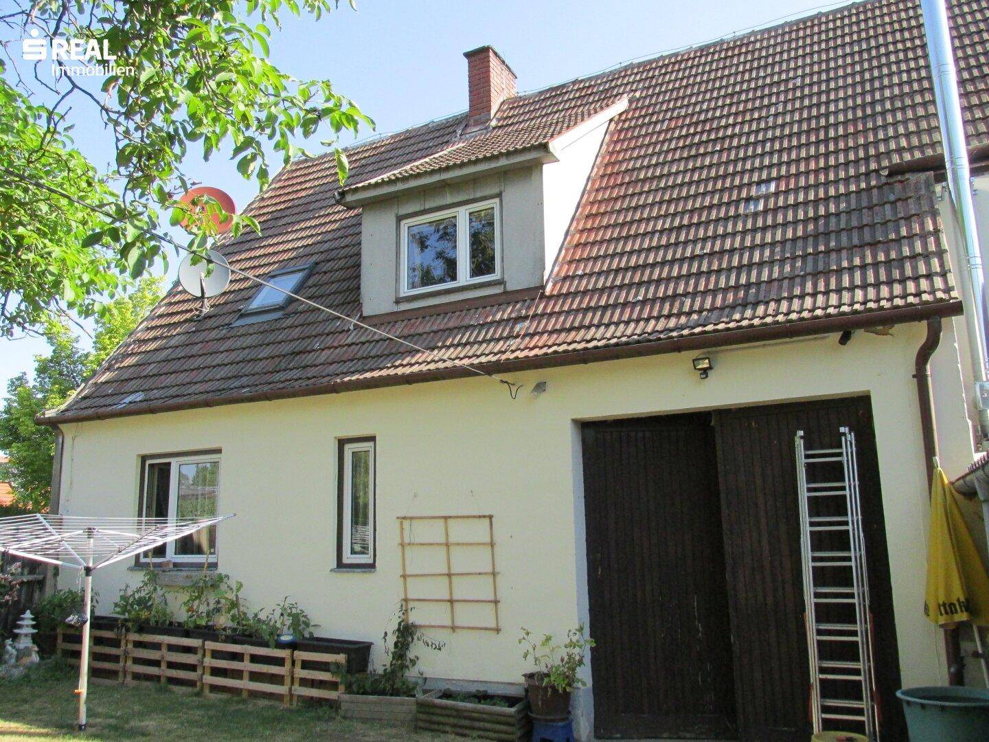 Rückansicht des Hauses mit Dachgaube, Satellitenschüsseln und Wäschespinne im gepflegten Garten.