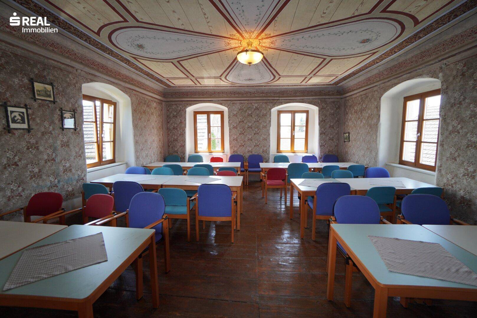 Historischer Speisesaal mit aufwendig bemalter Decke und vielen Sitzgelegenheiten.