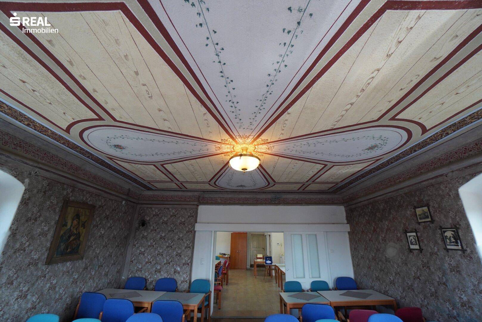 Historischer Raum mit bemalter Decke und Zugang zu einem angrenzenden Bereich.