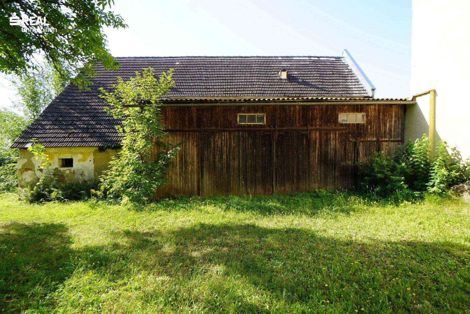 Rustikales Nebengebäude mit Holzwänden und Ziegeldach, umgeben von grüner Wiese.