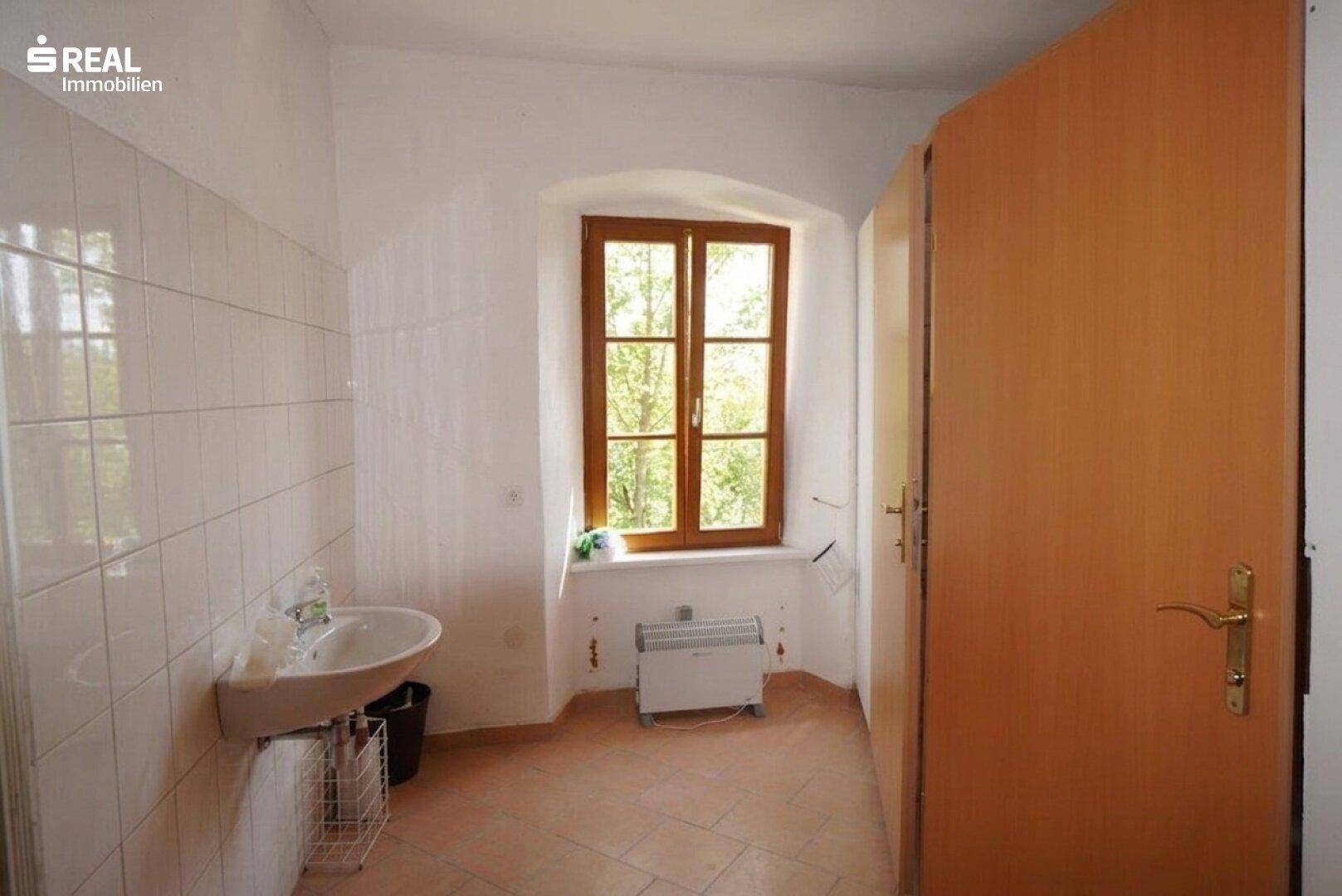 Kleiner Waschraum mit Waschbecken, Fenster und einfacher Fliesenwand.