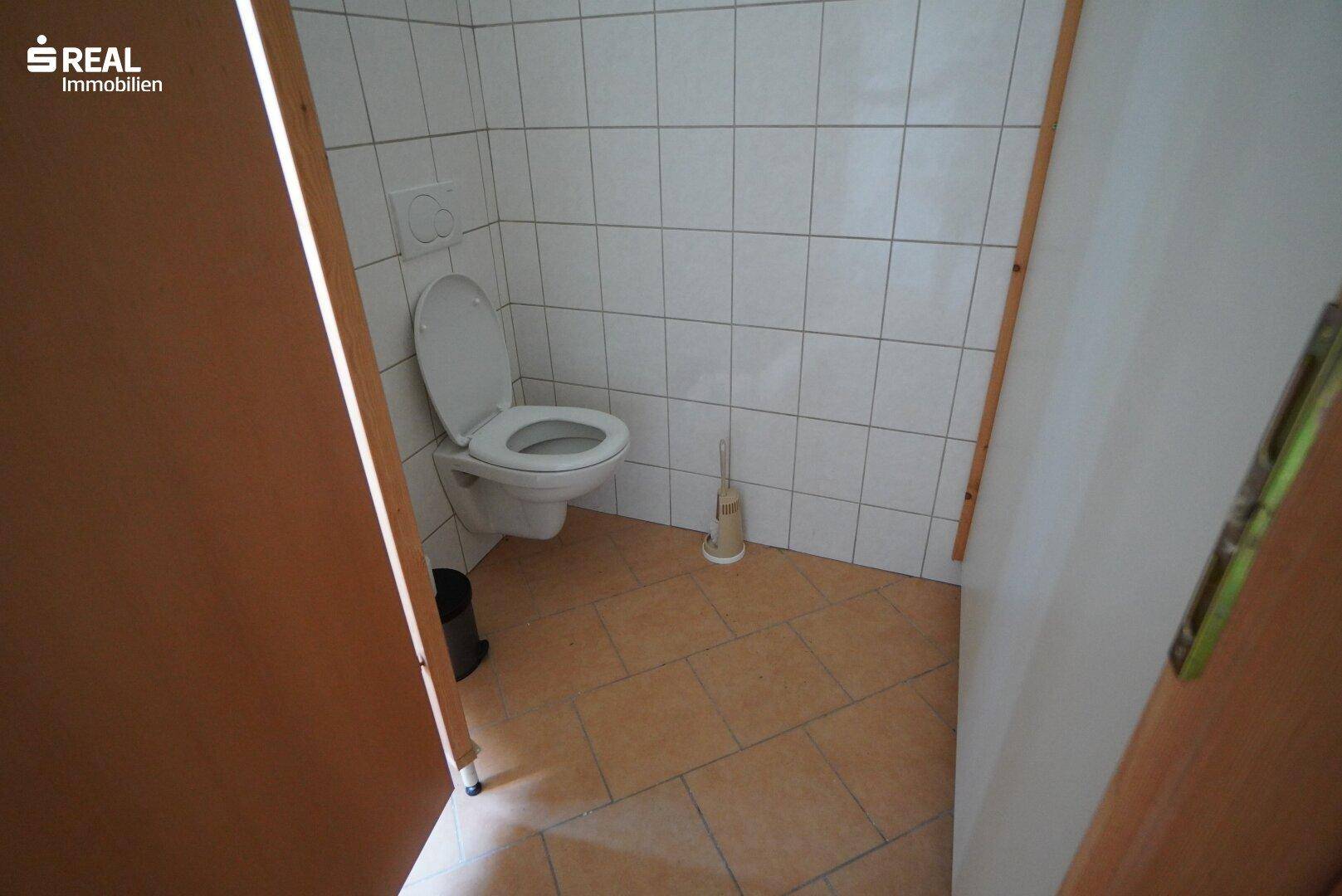 Separate Toilette mit Wand-WC und Fliesenboden.