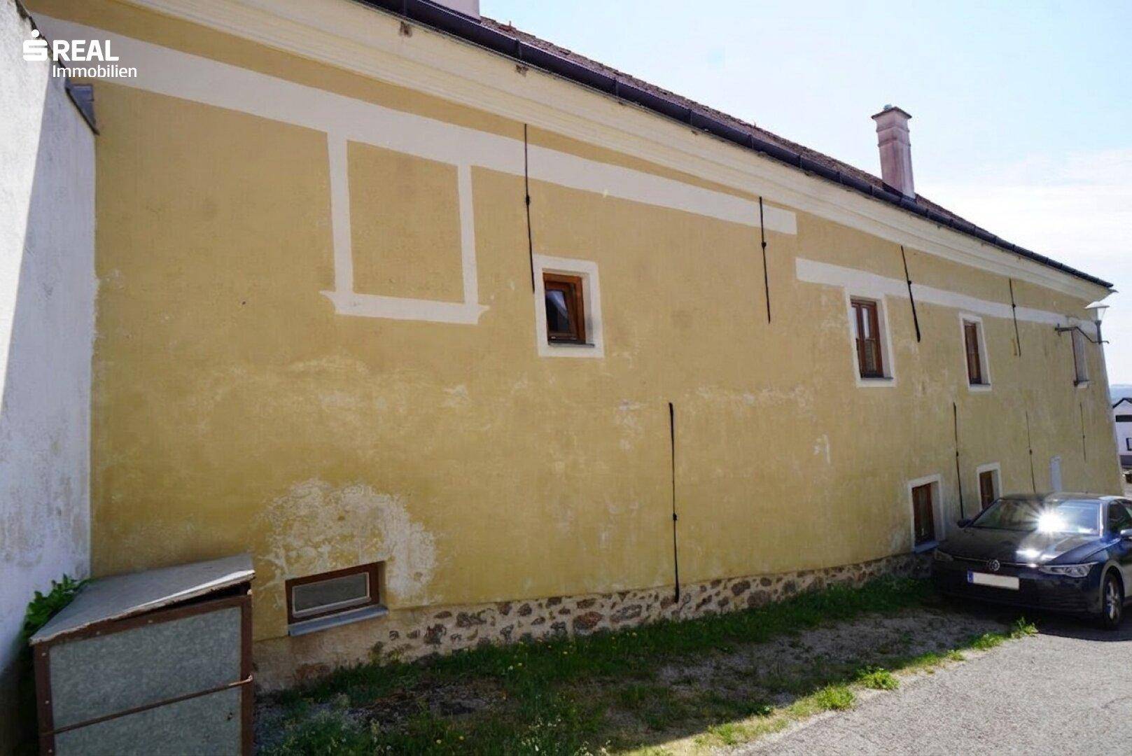 Seitenansicht des Gebäudes mit gelber Fassade, kleinen Fenstern und einem geparkten Auto.