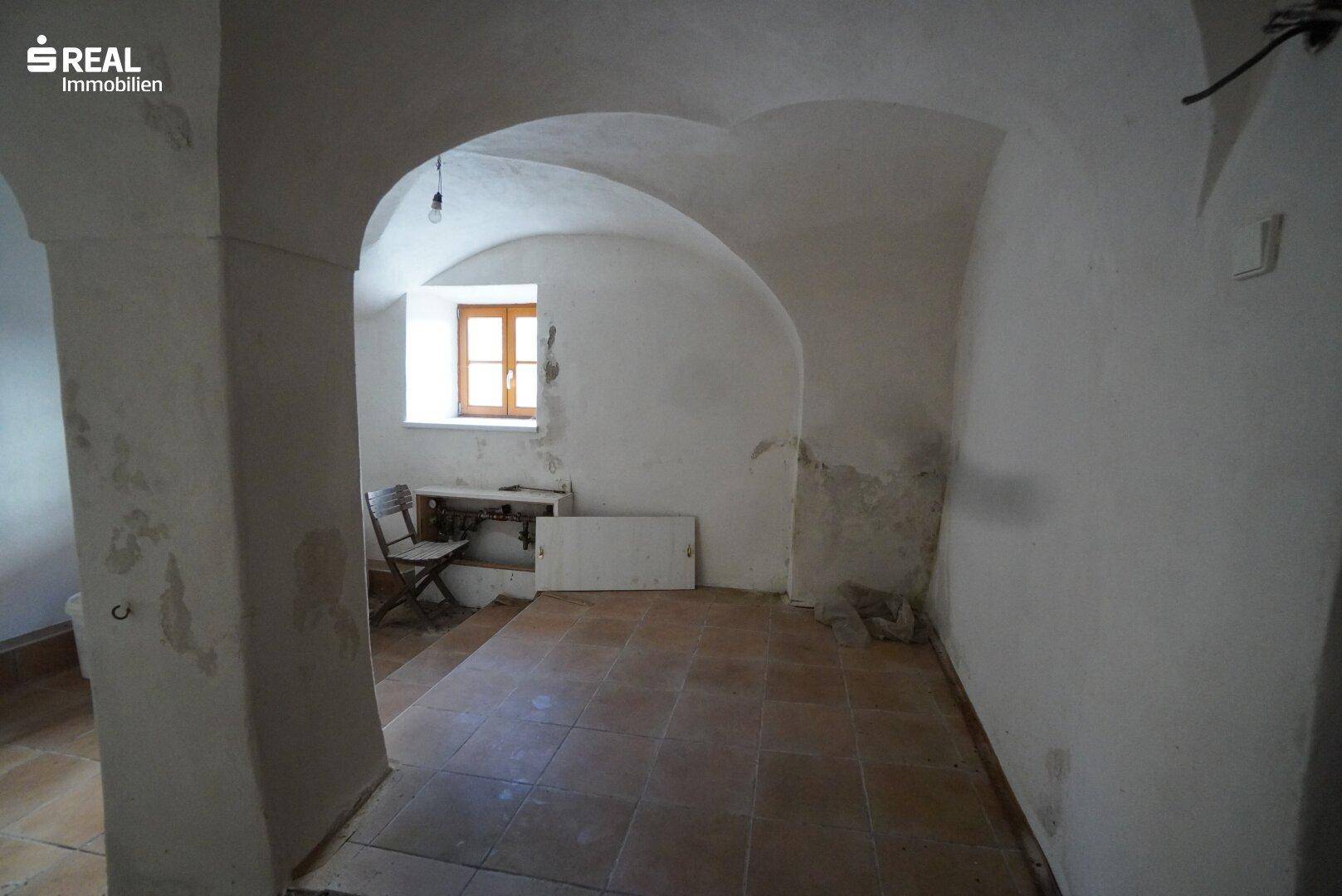 Geräumiger Raum mit Gewölbedecken, Terrakotta-Fliesenboden und einem Fenster.