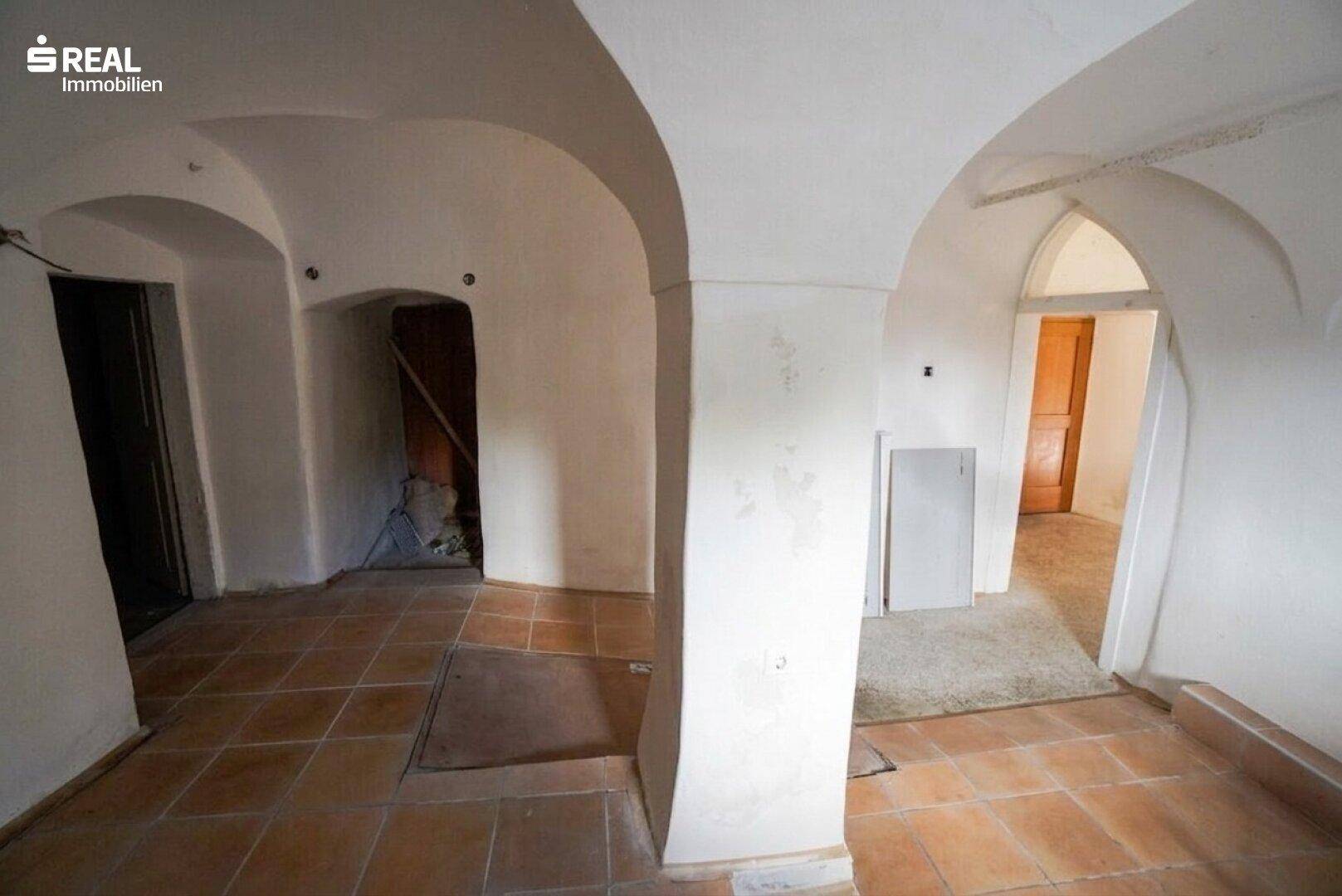 Großer Raum mit Gewölbedecken, Terrakotta-Fliesenboden und mehreren Türöffnungen.