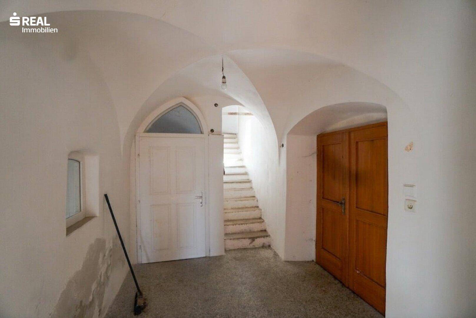 Historischer Flur mit weiß getünchten Wänden, Gewölbedecken und einer Steintreppe.