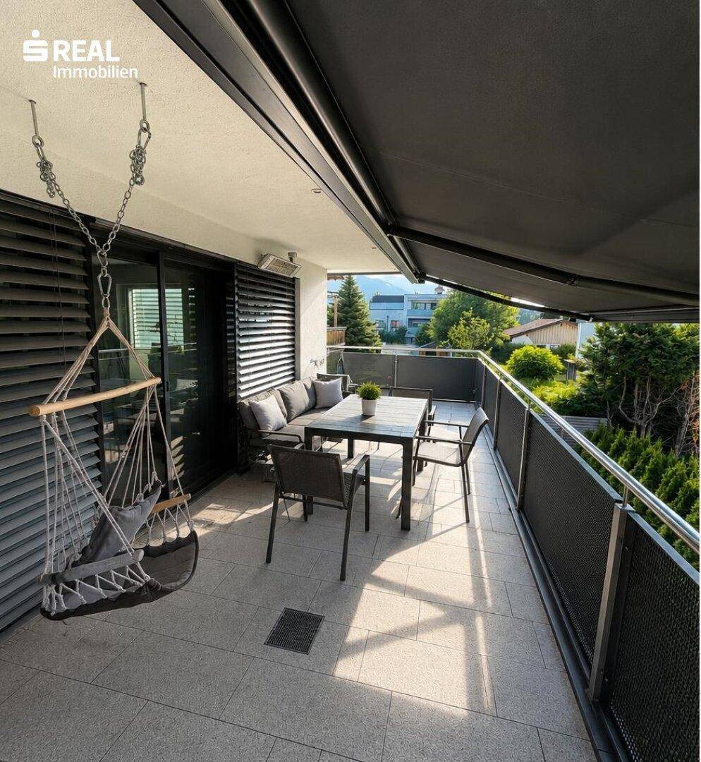 Geräumiger Balkon mit modernen Gartenmöbeln, Hängesessel und ausfahrbarer Markise.