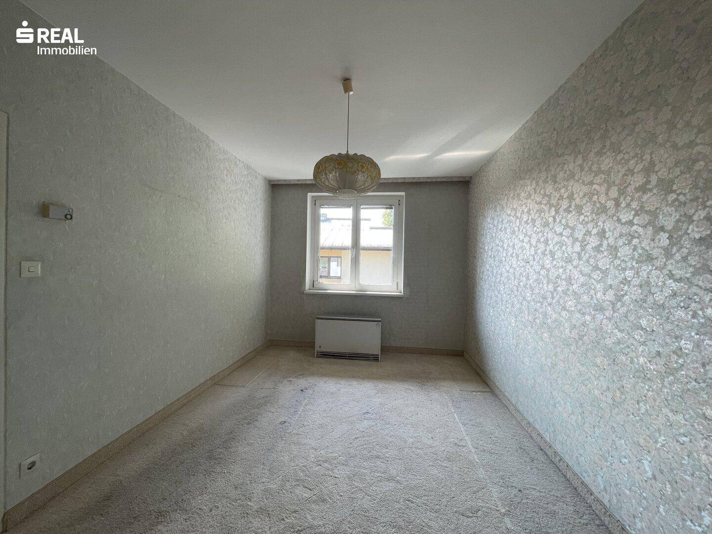 Schlafzimmer mit Teppichboden und einem Fenster, das Tageslicht in den Raum lässt.