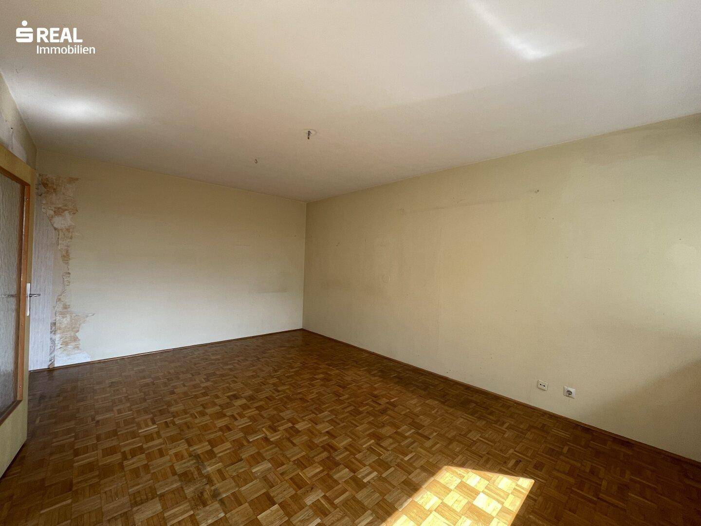 Leeres Wohnzimmer mit Parkettboden, bereit für individuelle Gestaltung und Renovierung.
