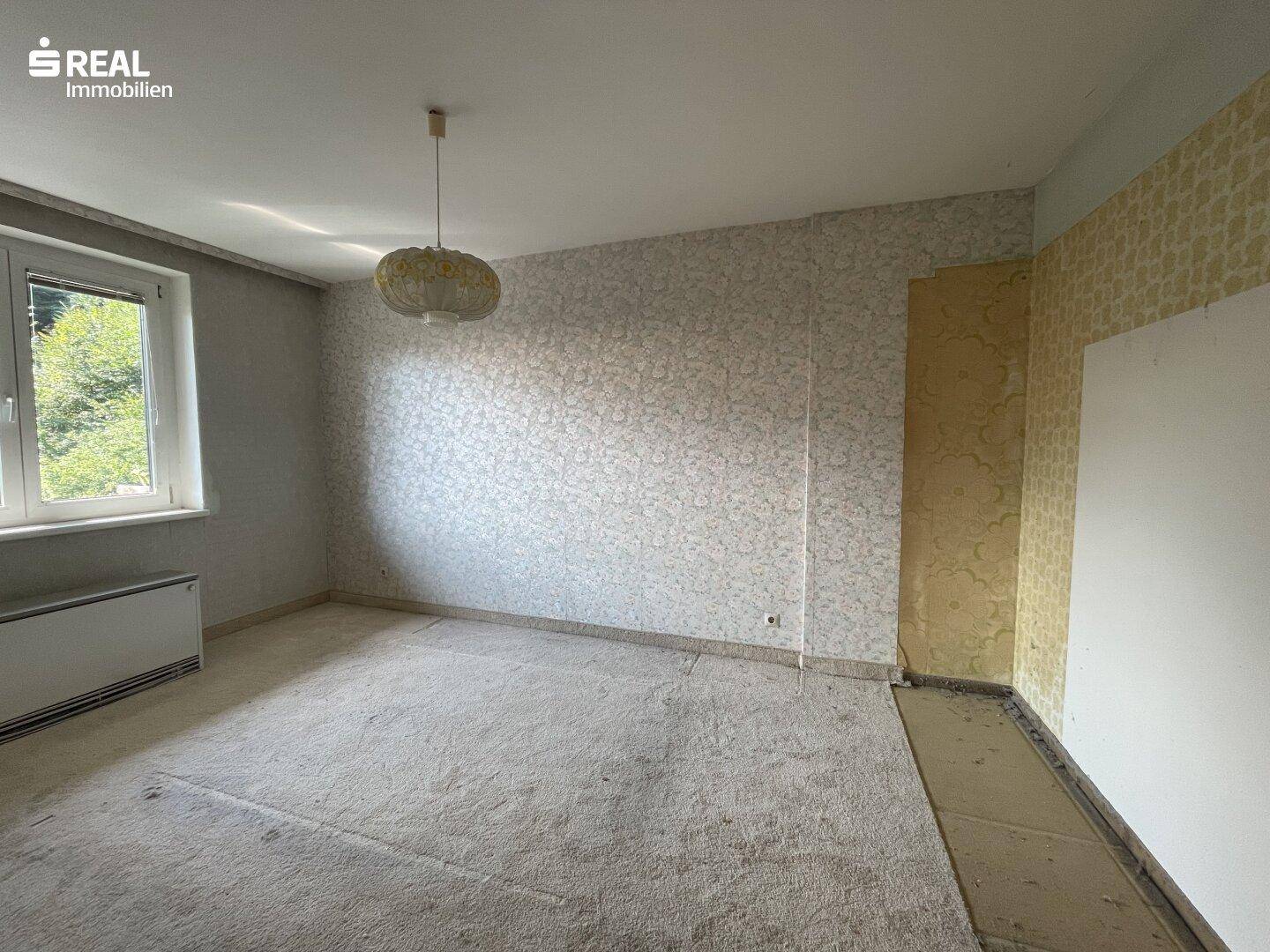 Schlafzimmer mit älterer Tapete und Teppichboden, ideal für eine Renovierung.