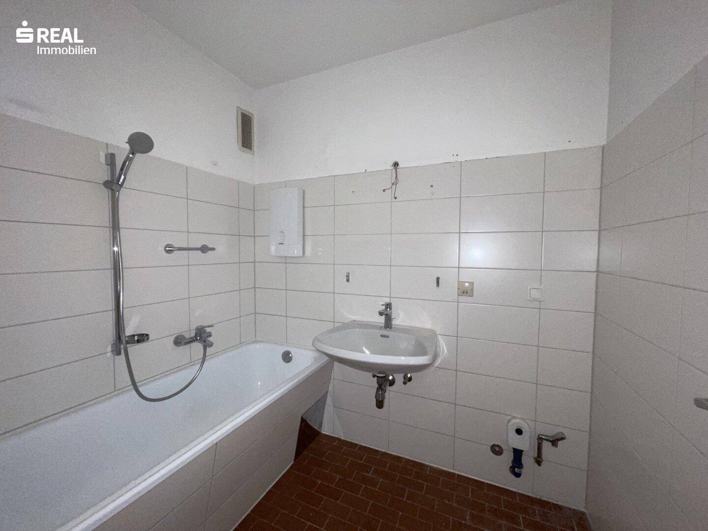 Badezimmer mit Badewanne, Waschbecken und weißen Fliesen, in gutem Zustand.