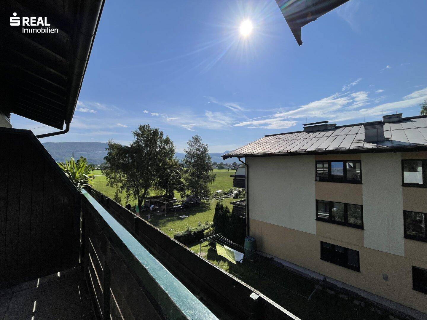 Sonniger Balkon mit weitem Blick über die grüne Landschaft und die umliegenden Berge.