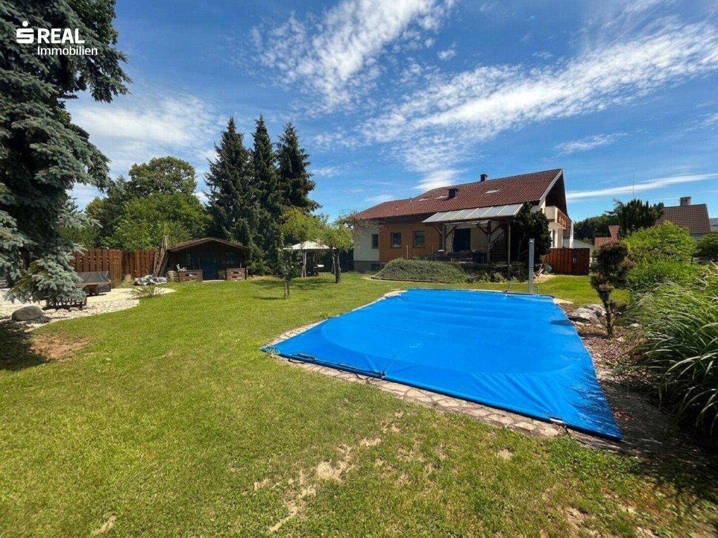 Hinterer Gartenbereich mit großem Rasen, abgedecktem Pool und dem Wohnhaus im Hintergrund.
