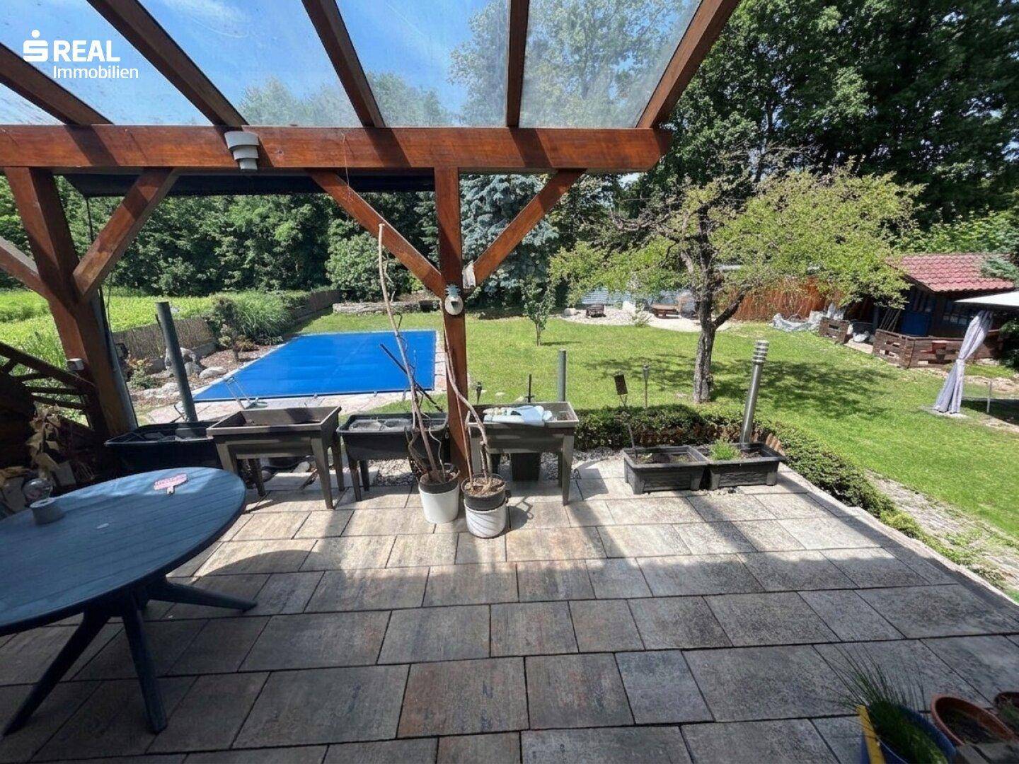 Überdachte Terrasse mit Steinplattenboden und Blick auf den Garten mit Pool.