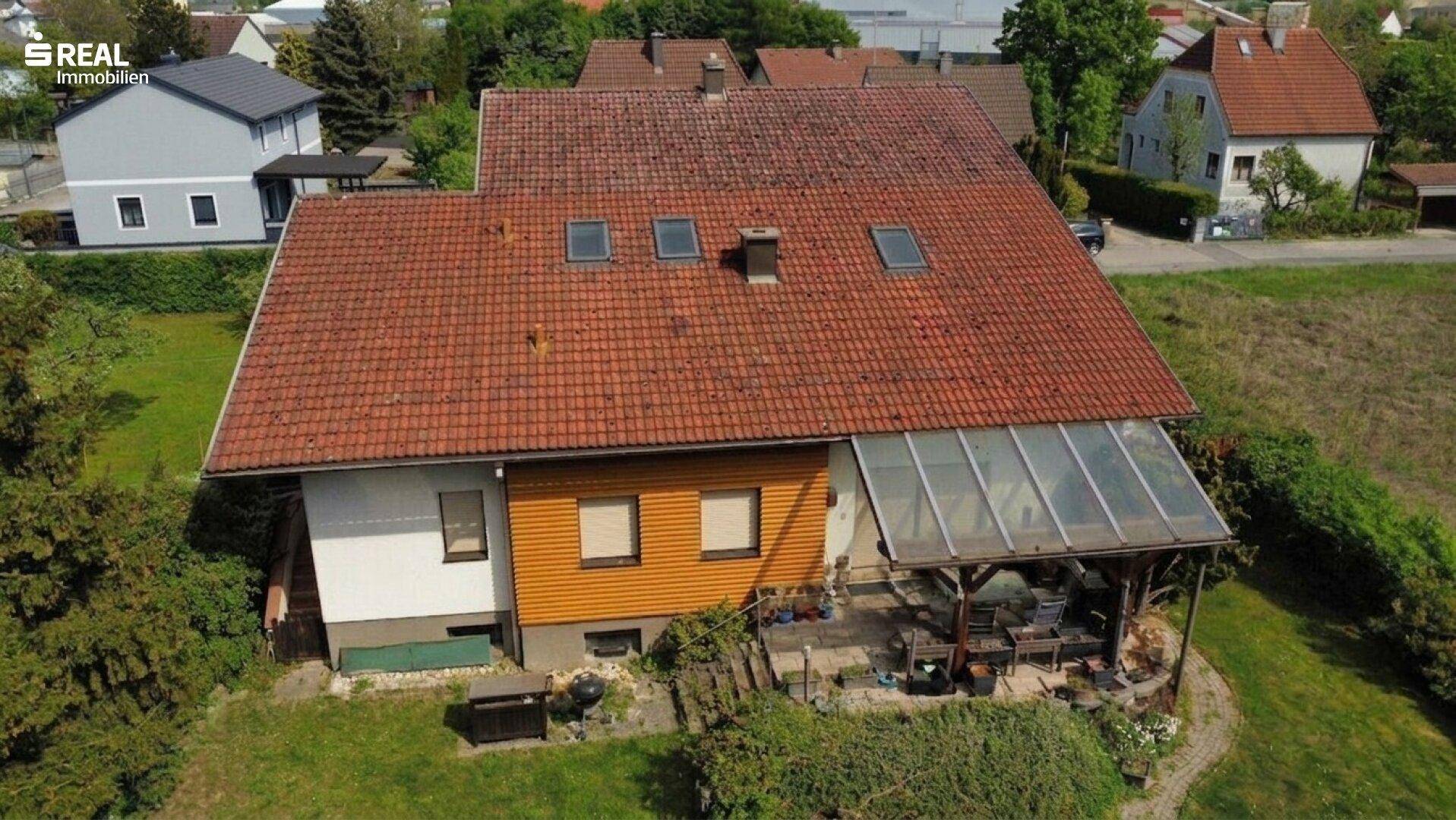 Luftaufnahme des Hauses mit rotem Ziegeldach, Wintergarten und großem Gartenbereich.