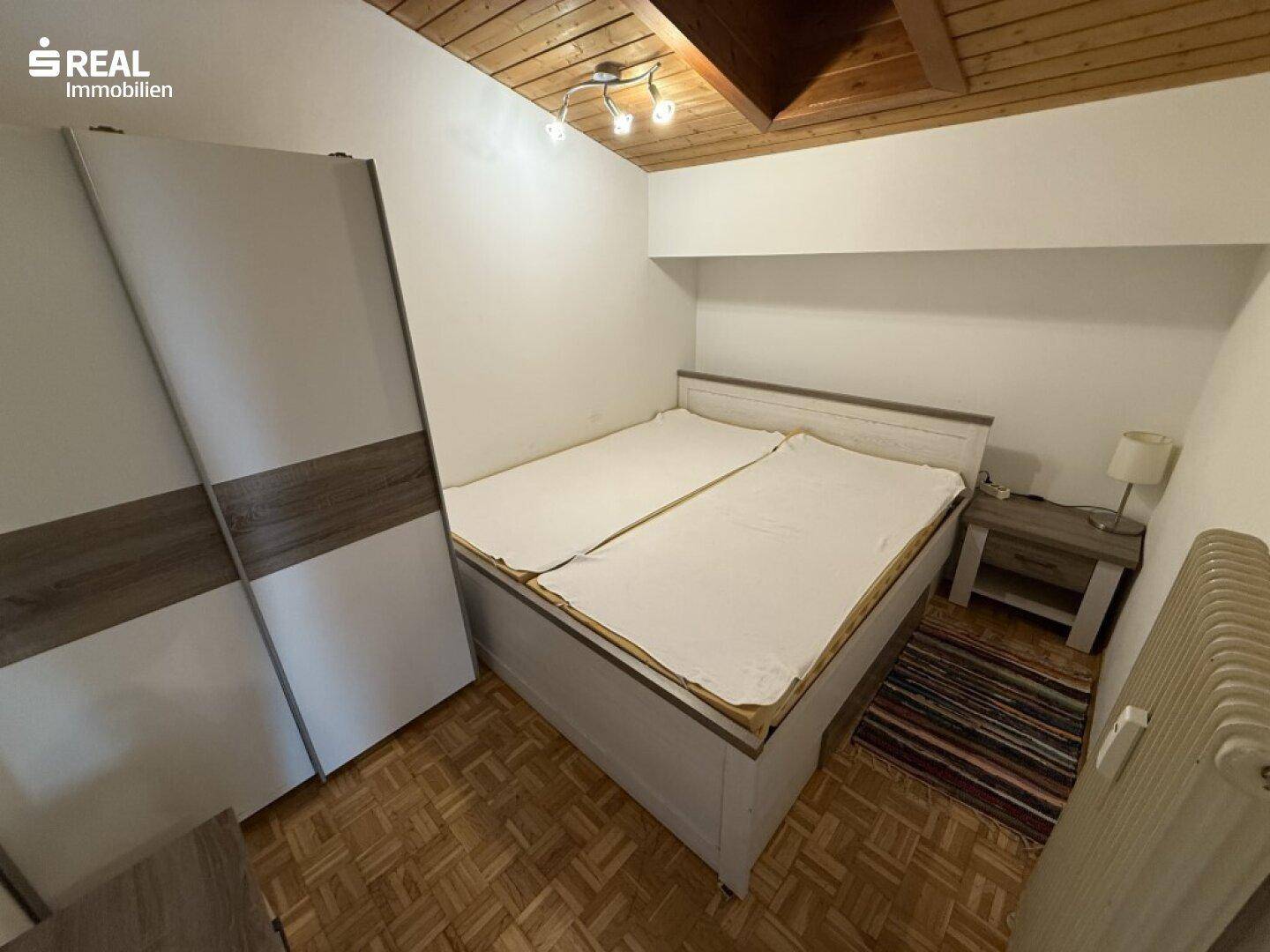 Gemütliches Schlafzimmer mit Doppelbett, Kleiderschrank und Holzbalkendecke.
