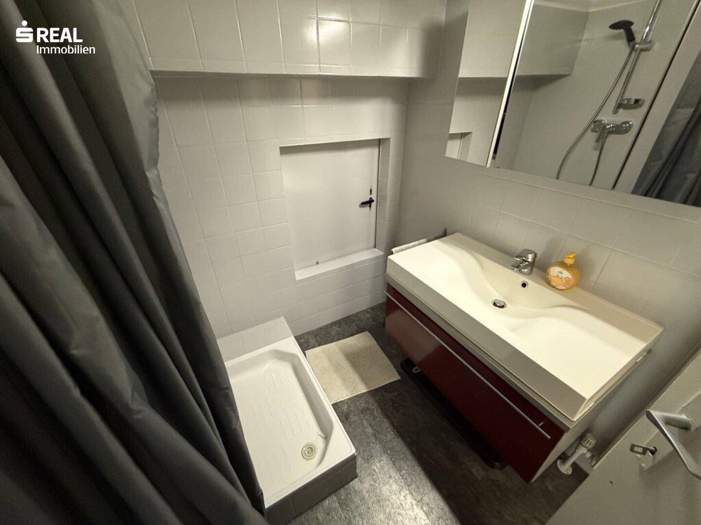 Funktionales Badezimmer mit Dusche, Waschbecken und weißen Fliesen.