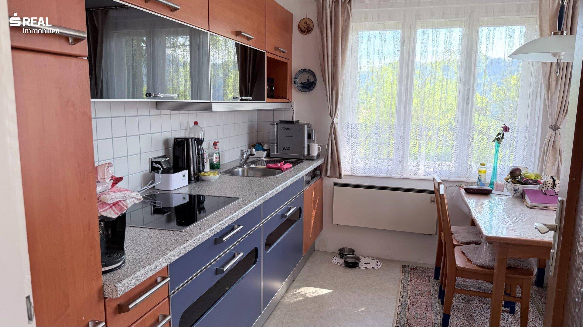 Gemütliche Küche mit Holzelementen, blauen Unterschränken und einem Essbereich am Fenster.