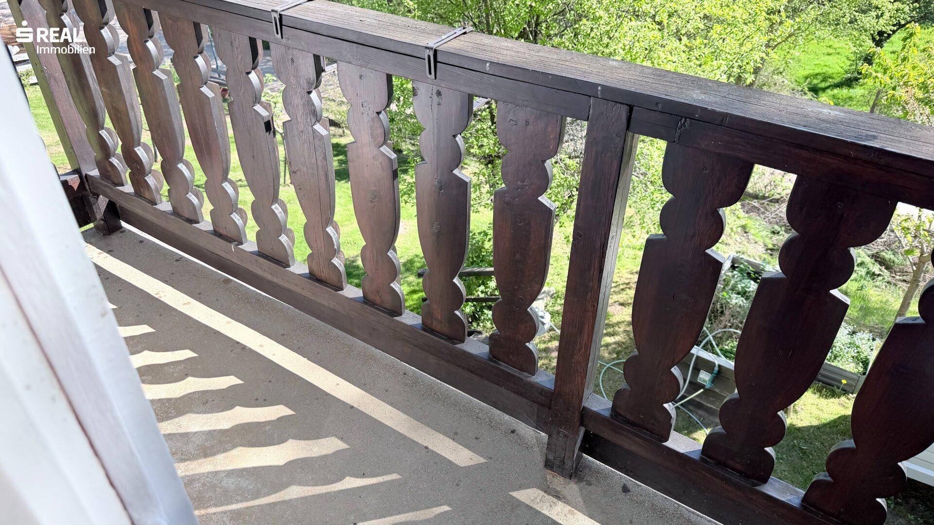 Balkon mit traditionellem Holzgeländer und Blick auf die grüne Umgebung.