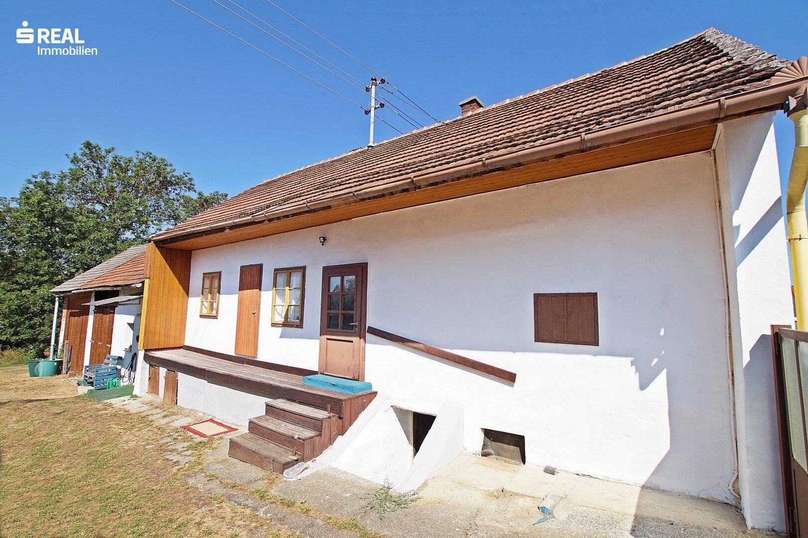 Ländliches Haus mit weißer Fassade, Holztüren und Zugang zum Keller.