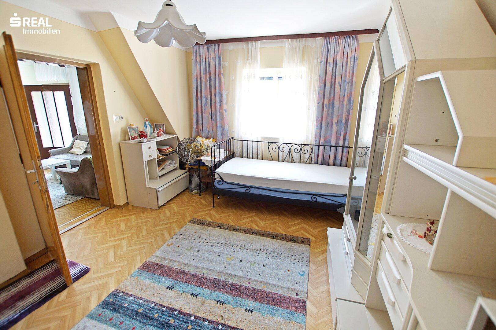 Helles Schlafzimmer mit Einzelbett, Holzparkett und schrägen Wänden im Dachgeschoss.